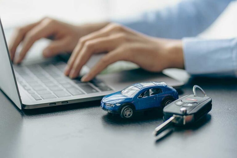 A family reviewing insurance documents beside a car and a laptop at a kitchen table.